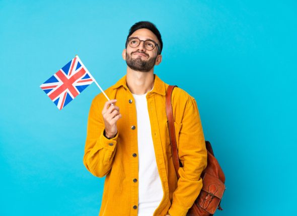 young-man-holding-united-kingdom-flag-isolated-yellow-wall-looking-up