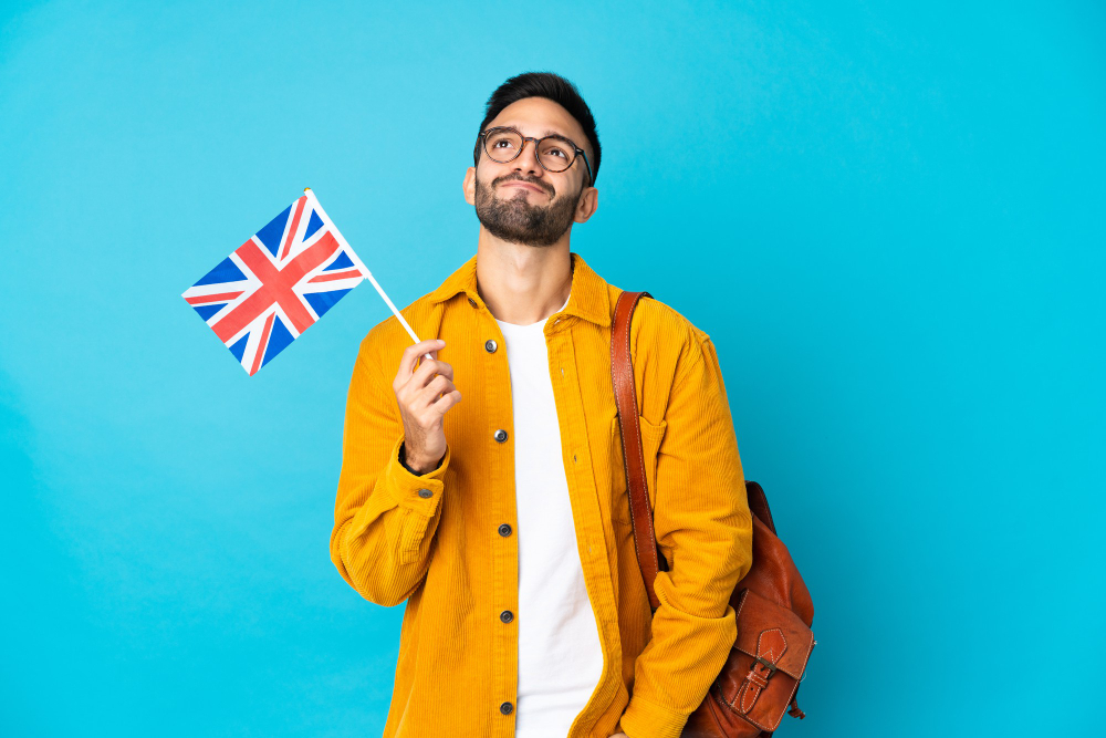 young-man-holding-united-kingdom-flag-isolated-yellow-wall-looking-up